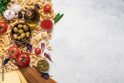 Italian food background. Variety of pasta, tomatoes, olive oil, tomato and pesto sauce, red basil, garlic, cheese on light background. Mediterranean cuisine concept