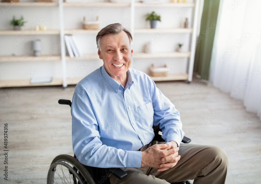 Fototapeta premium Portrait of joyful impaired senior man in wheelchair posing and smiling at home