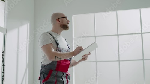 Bearded taskmaster writes ideas on clipboard in apartment