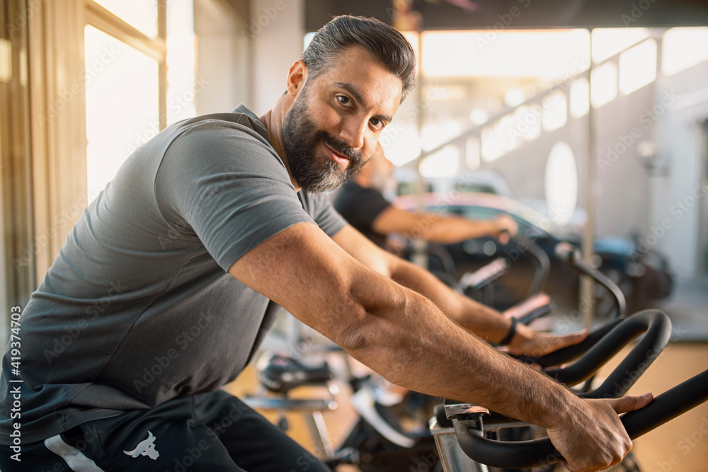 Portrait of a Young athletic man in sportswear doing cycling on exercise bikes at the gym