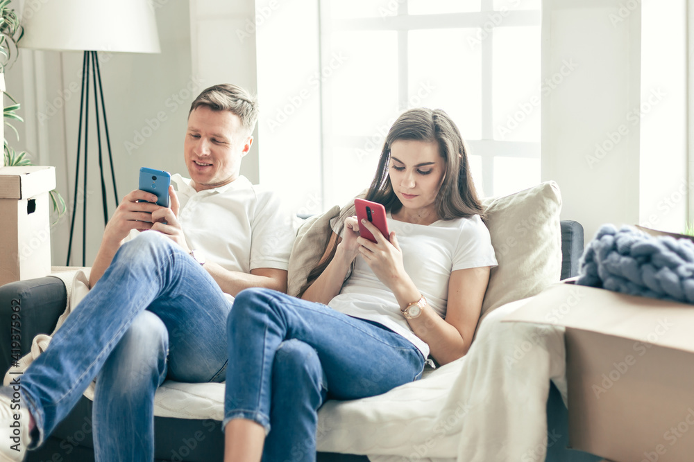 young couple with smartphones sitting on the sofa in a new apartment . young couple with smartphones sitting on the sofa in a new apartment .