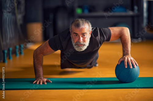 Strong and healthy middle-aged man doing push-ups with a ball 