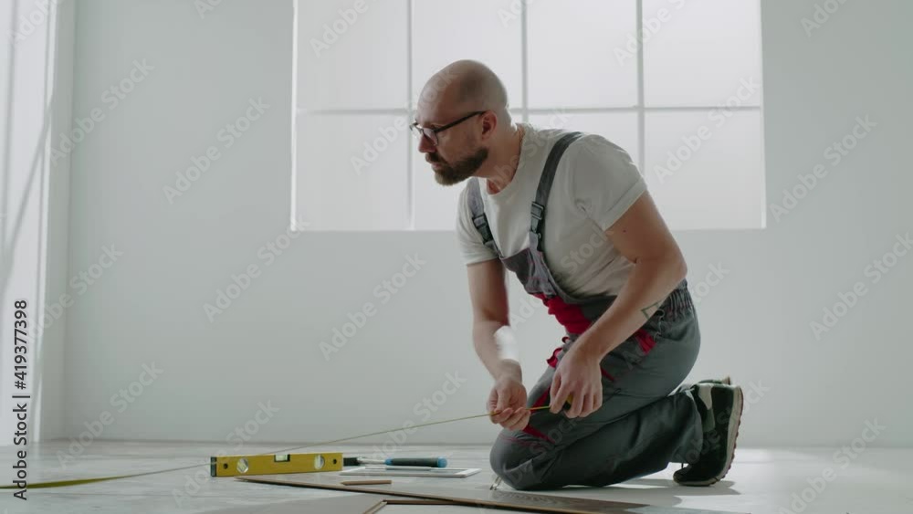Laborer with glasses measures parquet with retractable tape Laborer with glasses measures parquet with retractable tape