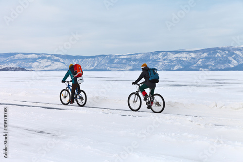 Baikal Lake. Two tourists on bicycles travel on the ice of the frozen Small Sea along Olkhon Island on a winter day. Healthy lifestyle. Ice travel and active vacation