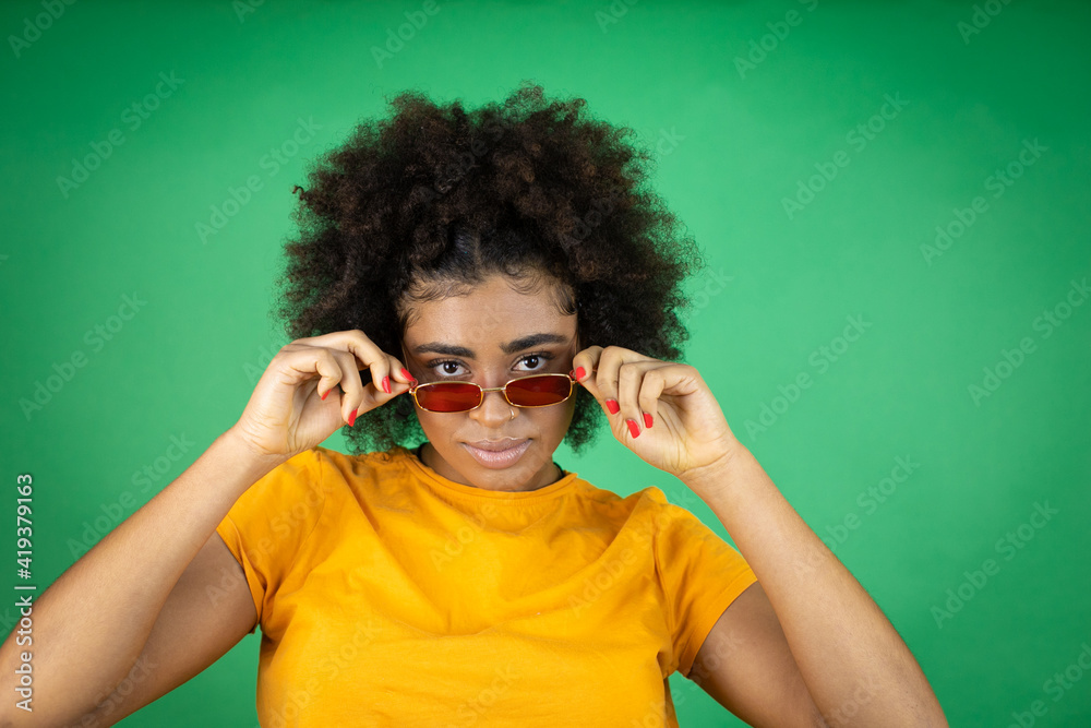 African american woman wearing sunglasses and orange casual shirt over green background with a happy face standing and smiling with a confident smile showing teeth