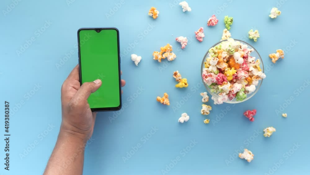 man hand using smart phone and eating popcorn 