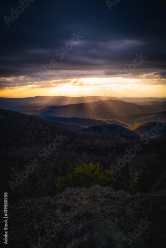 Sunset in Shenandoah National Park at Bearfence Mountain with golden crepuscular rays fanning out from a gap in the clouds.