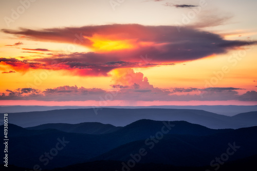 A anvil shaped cloud which is producing a small shaft of rain catches fire in the sunset light over the Blue Ridge Mountains.
