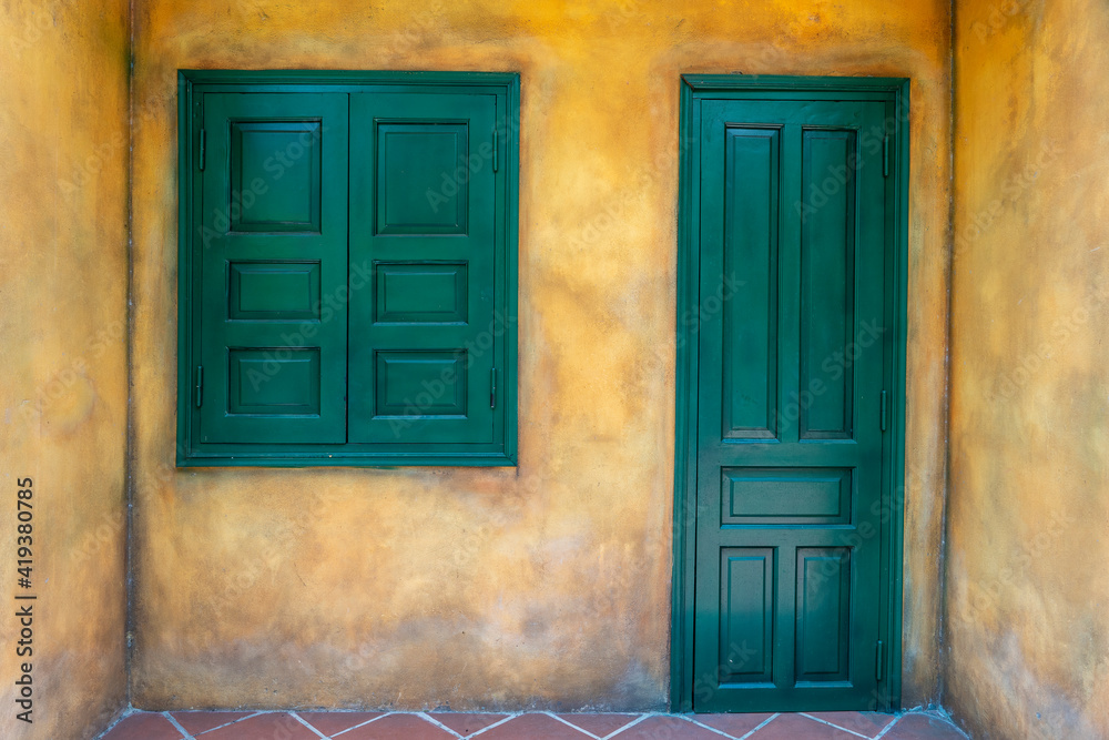 Closed green wooden door and window on old yellow wall, Hoi An, Vietnam