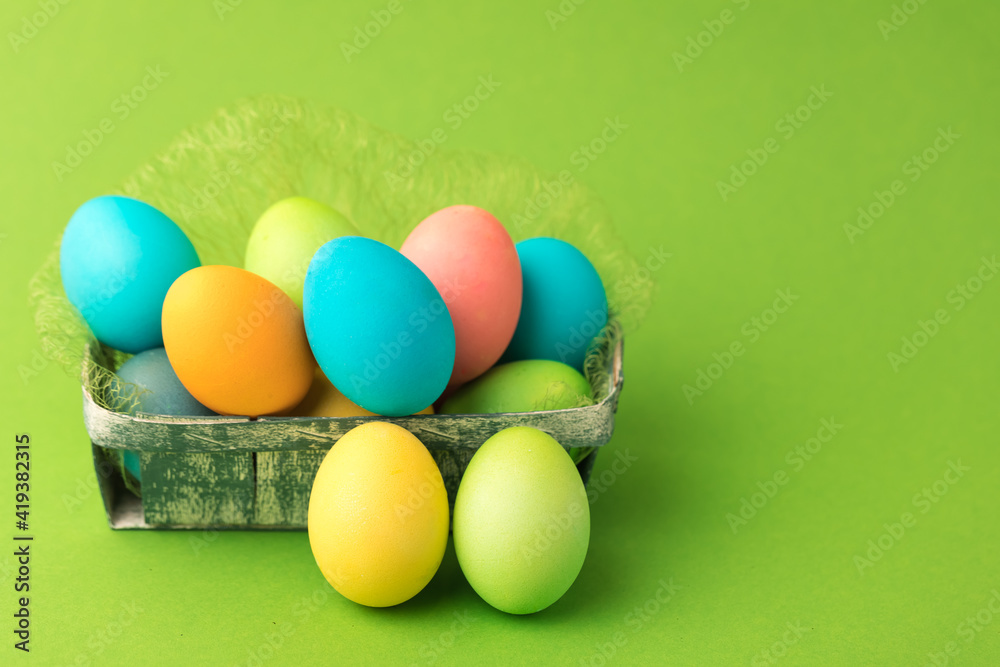 Multicolored chicken eggs are collected in a wicker basket. The concept of Easter. Green background