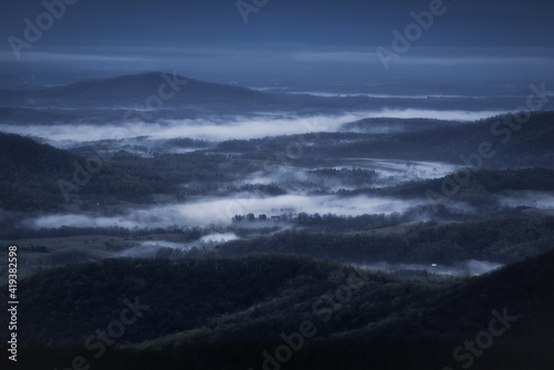 White mist fills the rural countryside of Virginia on a dark and moody, blue morning viewed from Shenandoah National Park.