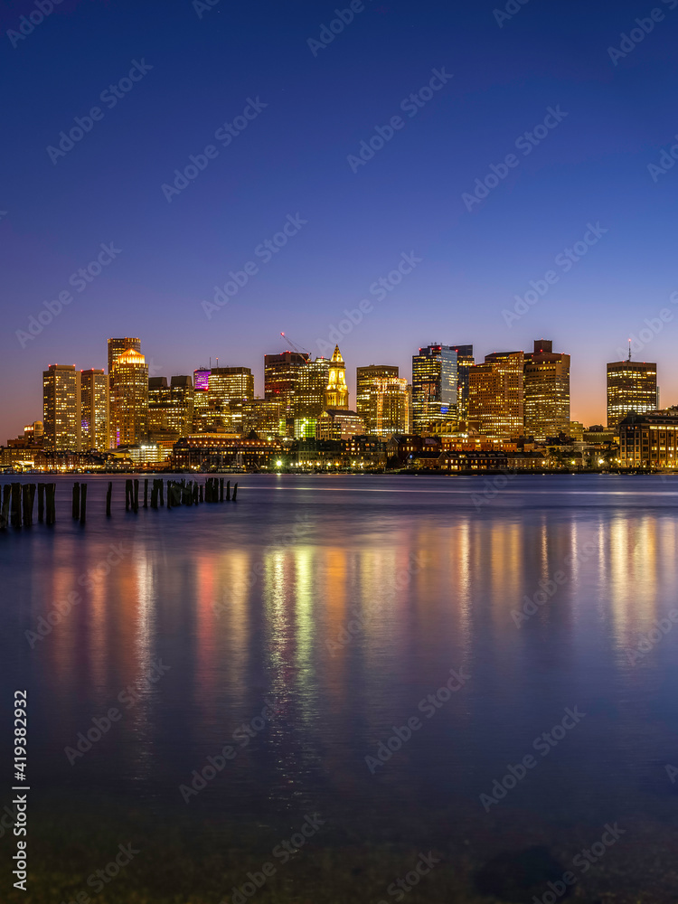 Boston Nightscape Skyline and Weathered Pier with Damaged Pilings. Harmony of Nature, Civilization, and Reflections of Lights and Time.