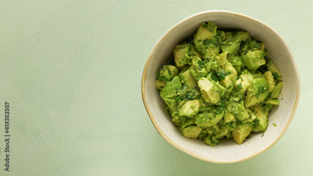 Bowl of freshly made chunky guacamole on bright green background with copy space for text, top view. Bowl of freshly made chunky guacamole on bright green background with copy space for text, top view.