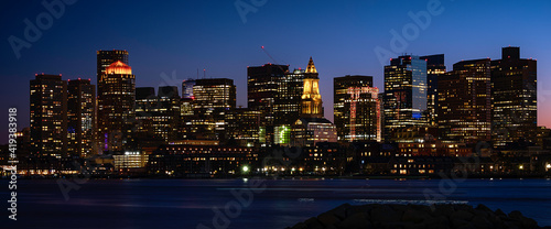 Panoramic Night Cityscape Boston Skyline over Boston Harbor. Dark Twilight Modern City Photo with Water Reflections.