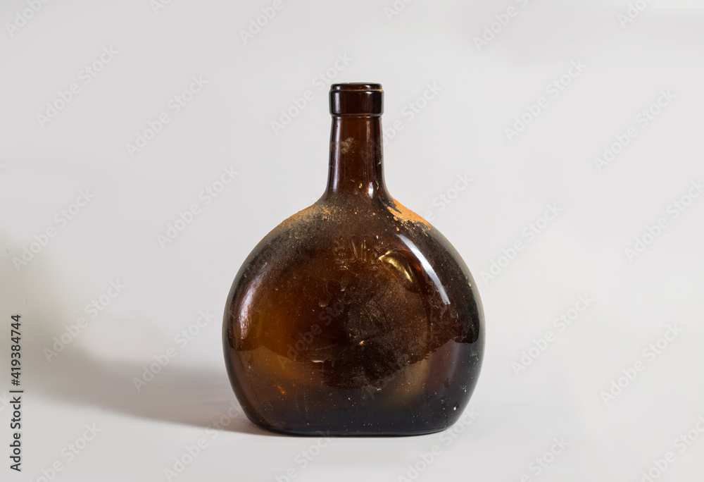 An old dirty bottle with an alcoholic drink on a light background An old dirty bottle with an alcoholic drink on a light background