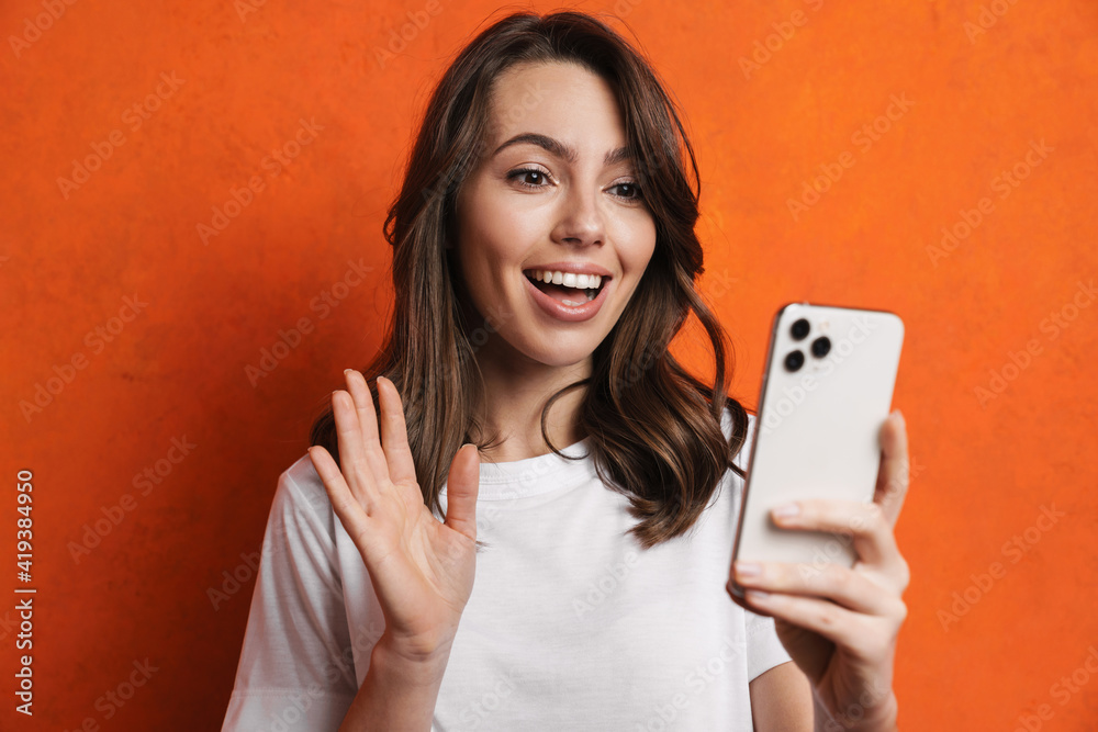 Cheerful charming girl waving hand and using mobile phone Cheerful charming girl waving hand and using mobile phone