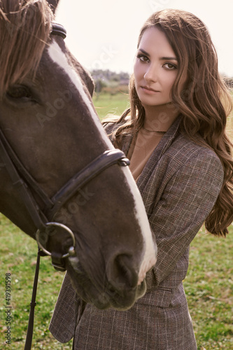Beautiful brunette woman in an elegant checkered jacket with a horse © micro