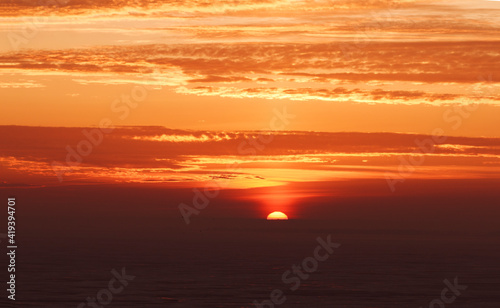 late beautiful sunset with clouds, sun goes down behind dark horizon, natural beauty background