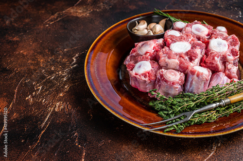 Fresh uncooked beef Oxtail cut Meat on rustic plate with herbs. Dark background. Top view. Copy space