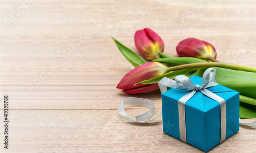 A gift and tulips on a wooden background. Spring flowers and a gift box. Red tulips and blue packaging.