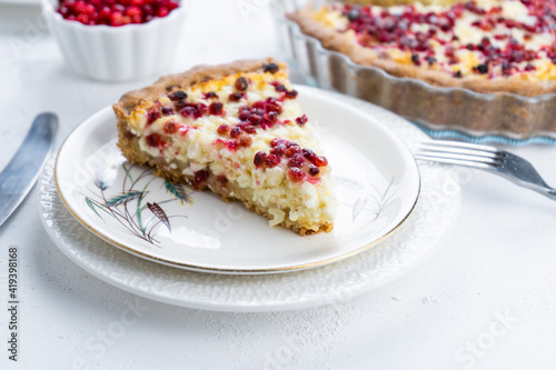 Curd tart with red lingonberries. Open round pie with berries on a white table. Baking food. A piece of cake on a plate.