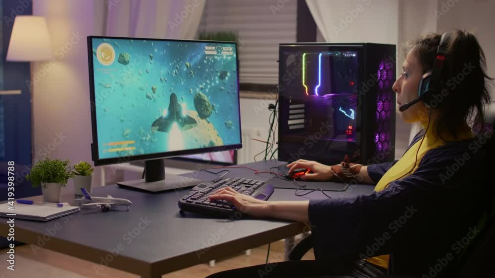 Gamer playing online space shooter video games using powerful computer and RGB keyboard. Player wearing headphones and talking into microphone with other players for winning online tournament Gamer playing online space shooter video games using powerful computer and RGB keyboard. Player wearing headphones and talking into microphone with other players for winning online tournament