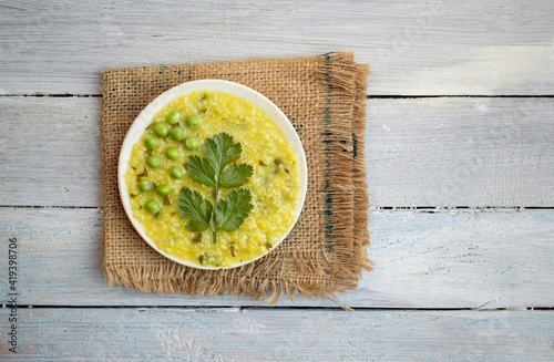 Dalia or Cracked Wheat Khichdi or Khichuri in a Plate with Coriander Leaves and Green Pea on Burlap Fabric Isolated on White Wooden Background photo