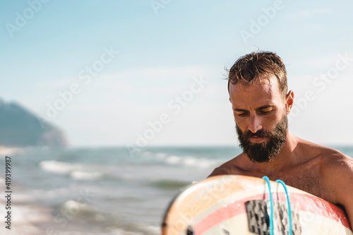 Surfer holding his surfboard walking on the beach - Hipster man training with surfboard - Lifestyle and freedom concept