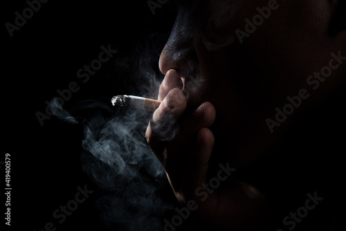 Close up young man smoking a cigarette black background