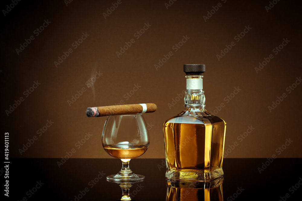 close up view of cigar, bottle of cognac and a glass aside on color back. close up view of cigar, bottle of cognac and a glass aside on color back.