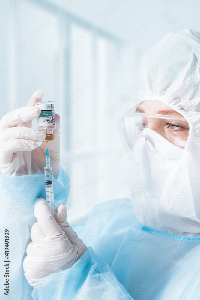 NO LOGOS OR TRADEMARKS! SELF MADE LABELS! Close up view of doctor with an ampule of covid vaccine and syringe on blue back NO LOGOS OR TRADEMARKS! SELF MADE LABELS! Close up view of doctor with an ampule of covid vaccine and syringe on blue back