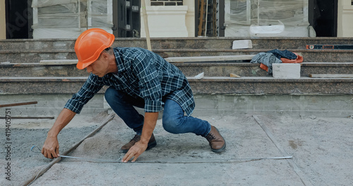 Builder measuring ground with industrial measuring tape on construction site