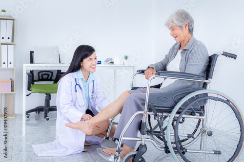 Female doctor examining senior woman's leg iwhile sitting on wheelchair. Elderly patient care and health care, medical concept.