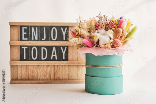 A beautiful bouquet of dried flowers and a wood stand with the inscription Enjoy today