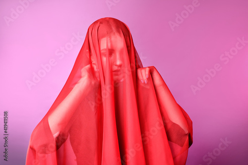 young girl wrapped face in red cloth. pink background