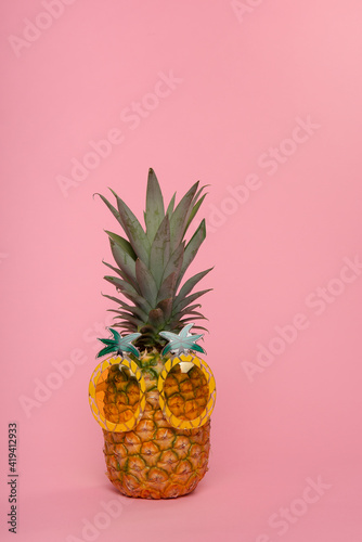 Funny pineapple with pineapple shaped glasses on a pink background