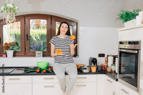 woman in kitchen. Woman sitting on the kitchen table in the kitchen holding fruits and vegetables in her hands. Food blogger in the kitchen. To eat healthy food. Cooking with joy. White home kitchen