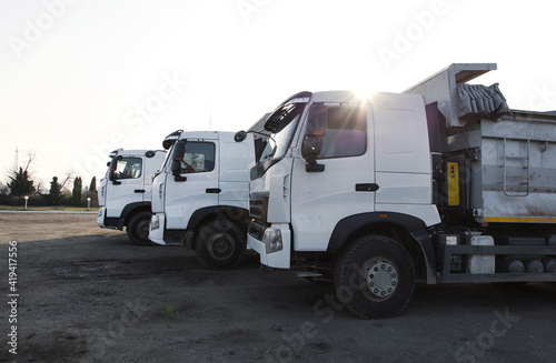 three dump trucks with white clean cabins stand next to each other. Delivery, logistics, construction, commercial transport. Sun rays. Copy space
