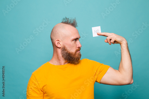 Bearded european man in yellow shirt isolated on turquoise background holding no strong man serious face