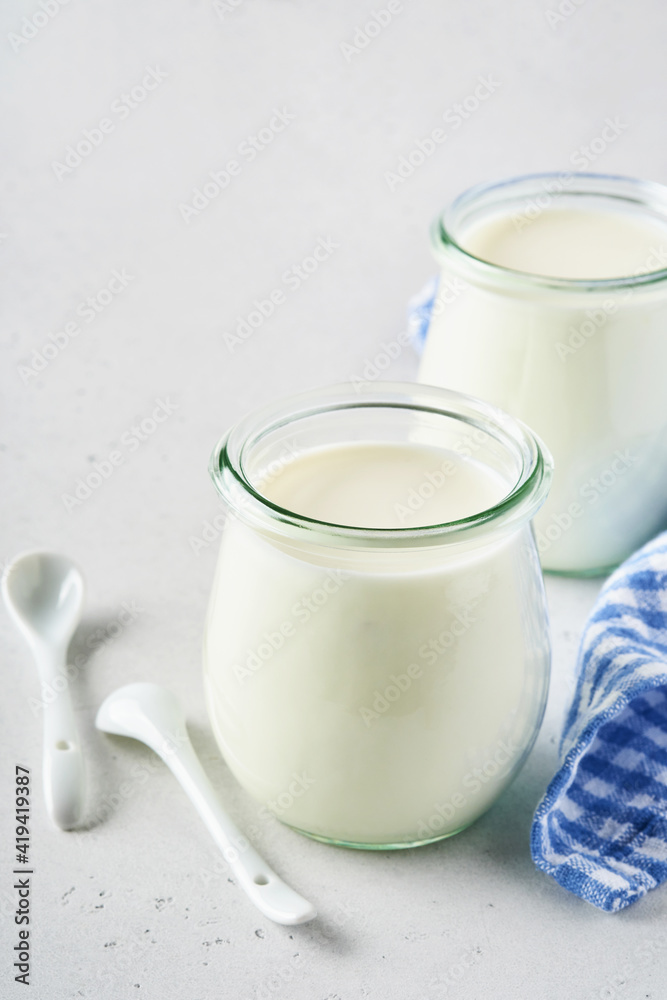 Sour cream or natural yogurt in a glass jar with spoons, health and diet concept on light gray slate background. Sour cream or natural yogurt in a glass jar with spoons, health and diet concept on light gray slate background.
