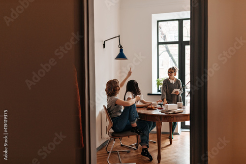 Gorgeous girls sitting at table and laughing in good day. Indoor shot of good-humoured friends spending time at home.