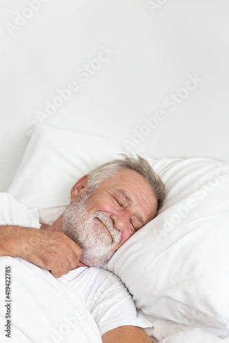 Senior retirement man sleeping happily in his white blanket bed in bedroom