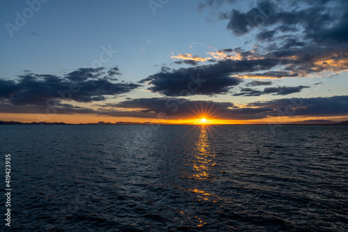 scenic and colorful sunset over the ocean with shimmering light on the waves and silhouette of mountains on the shore behind