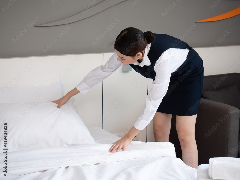 Beautiful Asian maid setting up the white pillow on the bedsheet in the hotel room. Cleaning in the hotel room. The concept of the hotel business. Beautiful Asian maid setting up the white pillow on the bedsheet in the hotel room. Cleaning in the hotel room. The concept of the hotel business.