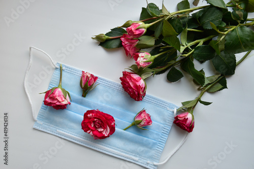 Fototapeta Naklejka Na Ścianę i Meble -  Fresh small rosebuds on the medical face mask and a bouquet of spring roses on the white table.