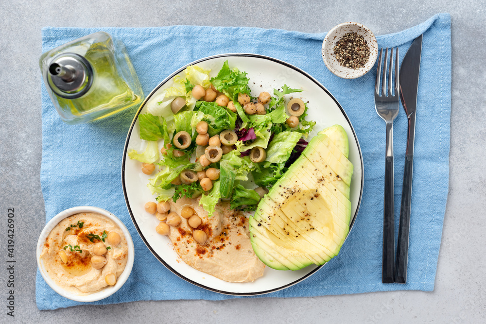 Chickpea avocado salad on a plate, Healthy vegan vegetarian salad with hummus, greens, chickpeas and large avocado half cut into slices. Top view Chickpea avocado salad on a plate, Healthy vegan vegetarian salad with hummus, greens, chickpeas and large avocado half cut into slices. Top view