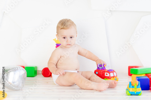 a small child a boy six months old plays with bright toys in a bright white room in diapers