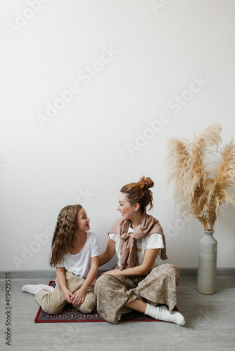 Mother and daughter look at each other sitting on the red carpet on the floor against the wall