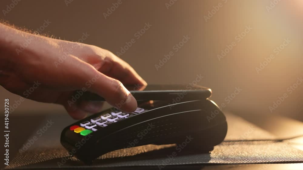 Pays by Contactless Mobile Phone to Credit Card System. Smartphone payment with tap wireless system in a small shop. Mobile payment concept - Young man pays by contactless phone to credit card system