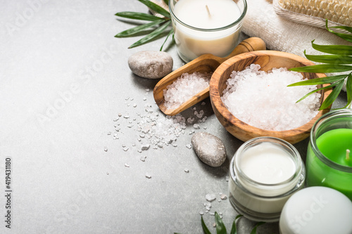 Spa product composition with cosmetics, sea salt, towel and palm leaves at stone table.